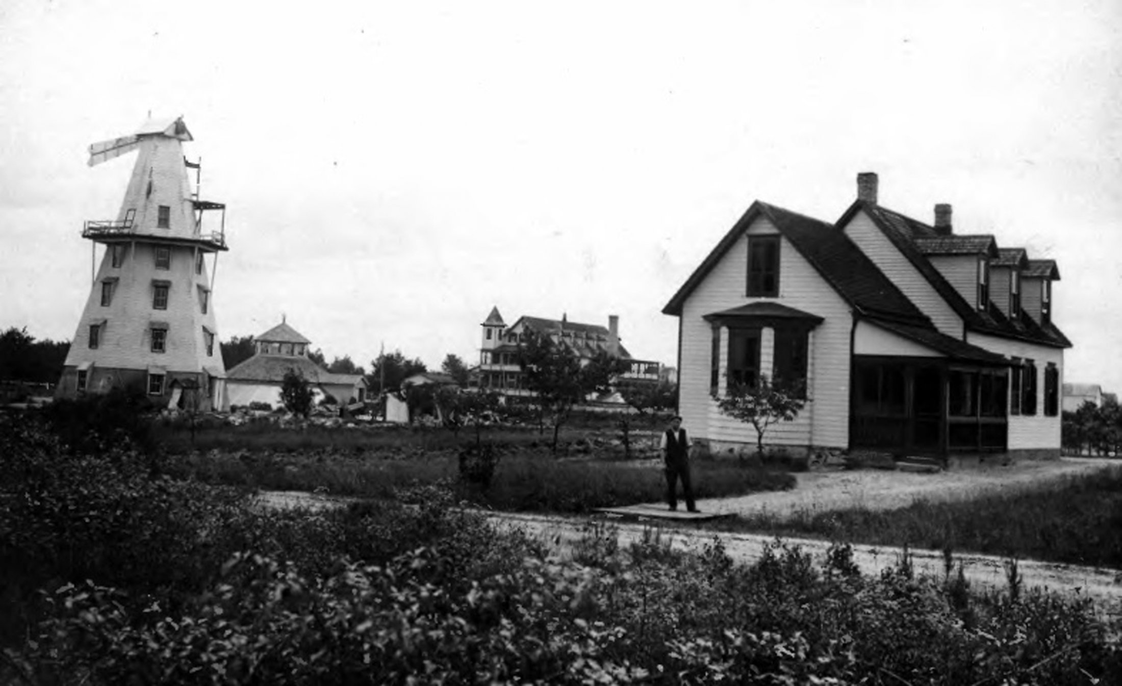 Egg Harbor City - Dr. Smith's house at 500 Washington Ave., Egg Harbor City. The hotel is clearly visible in the background, center. The building at the left may be a windmill- The man standing at the corner in front of the house is Lloyd Johnson